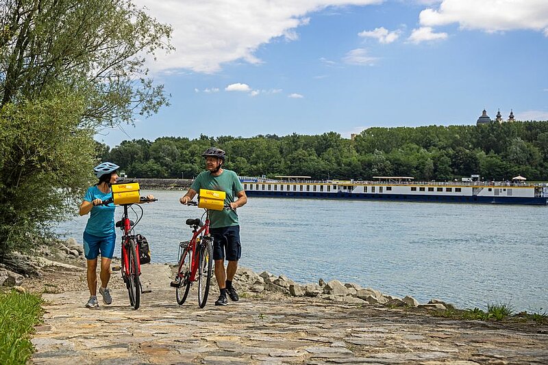 Radfahrer schieben ihre Räder am Donauufer