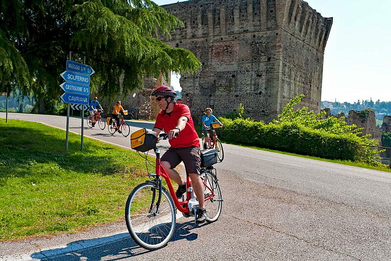 Radler fahren an Burgruine von Borghetto vorbei